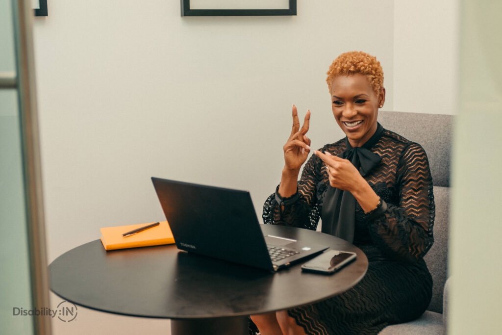 Young black woman with red hair and a laptop is using sign language to communicate on a video-conference