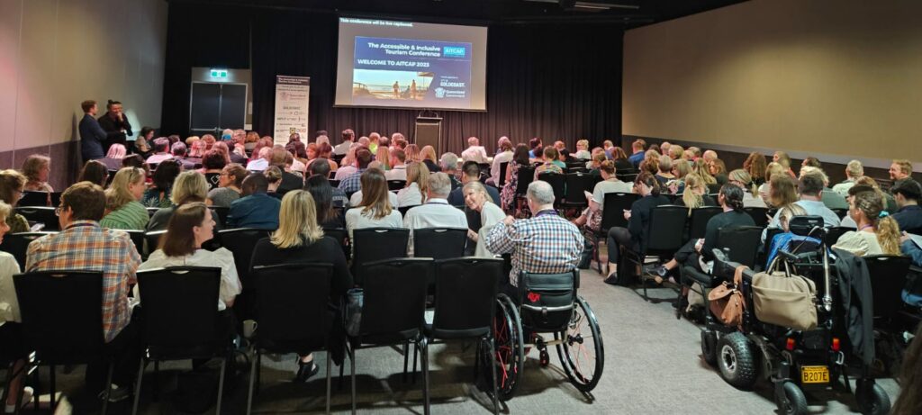 View from the back of the Main Room at AITCAP 2023 on the Gold Coast with attendees filling the room and a giant screen projecting slides above the stage.